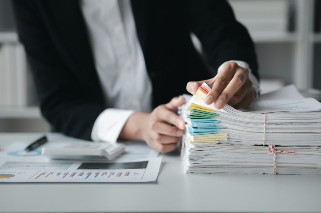 Businessman looking through stacks of papers on desk, corporate financial papers.